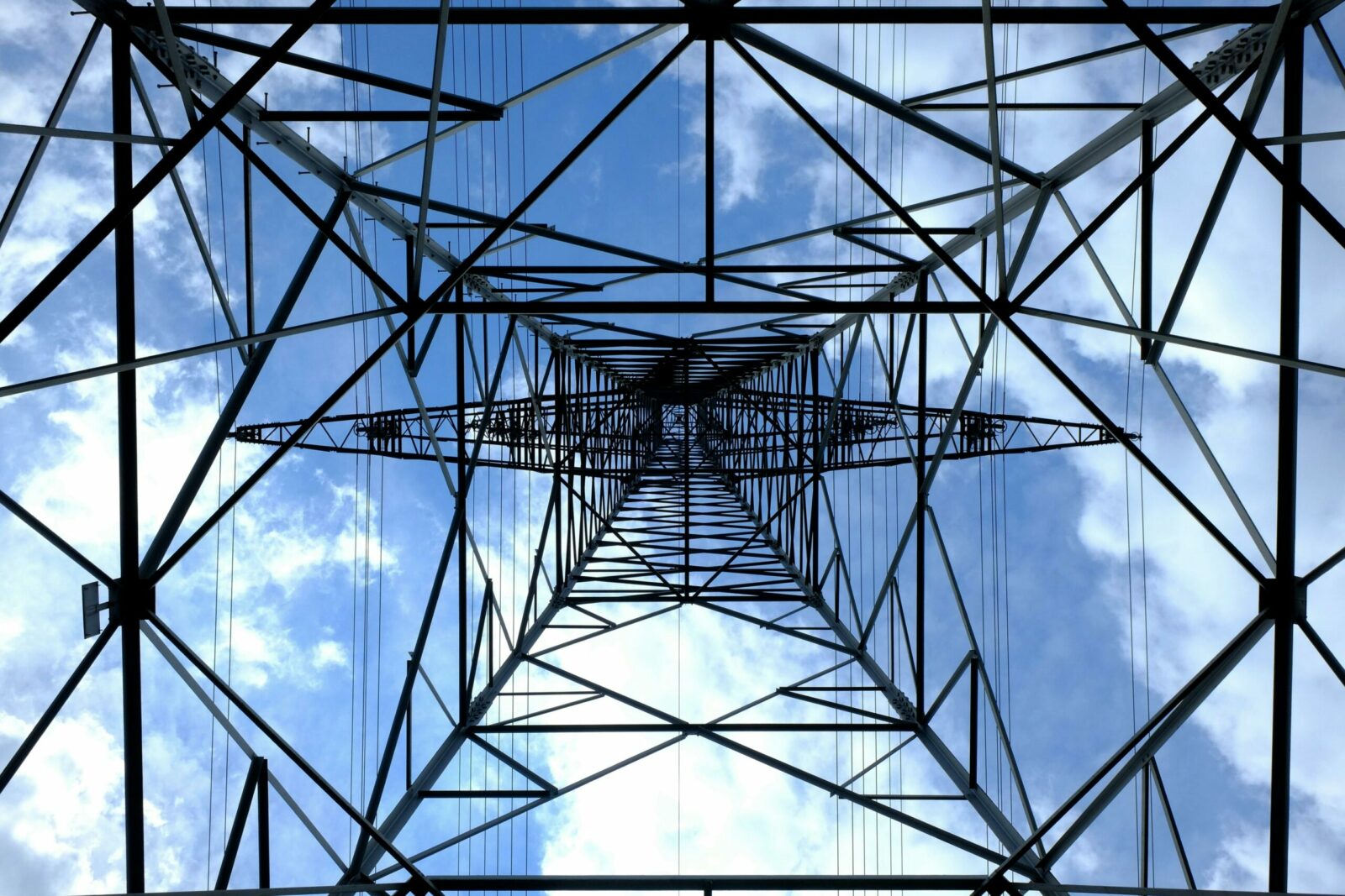 Looking up at a steel power pylon against a bright blue sky.